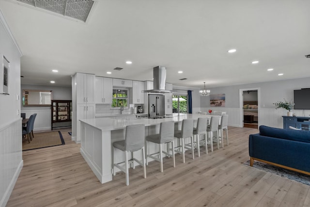 kitchen with a wainscoted wall, light countertops, visible vents, white cabinetry, and island range hood