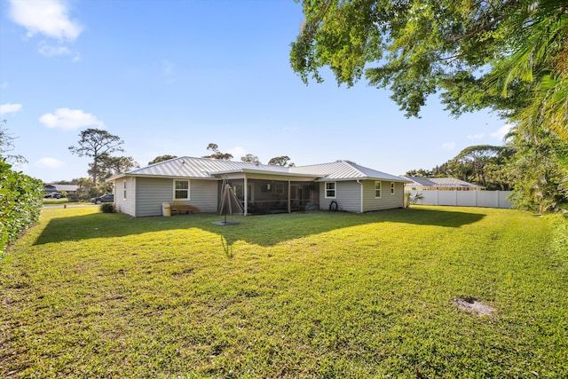 back of house with metal roof, a lawn, a fenced backyard, and a sunroom