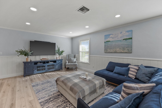 living area featuring light wood-style floors, wainscoting, visible vents, and crown molding