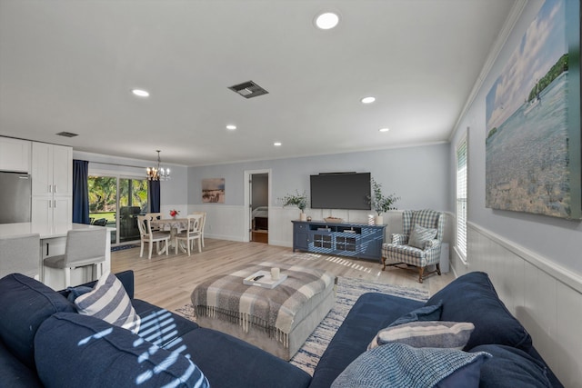 living area featuring light wood-style flooring, visible vents, a notable chandelier, and wainscoting