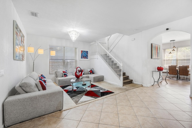 tiled living area featuring arched walkways, visible vents, stairway, a chandelier, and baseboards