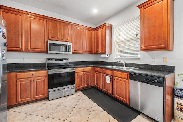 kitchen with appliances with stainless steel finishes, dark countertops, a sink, and light tile patterned floors