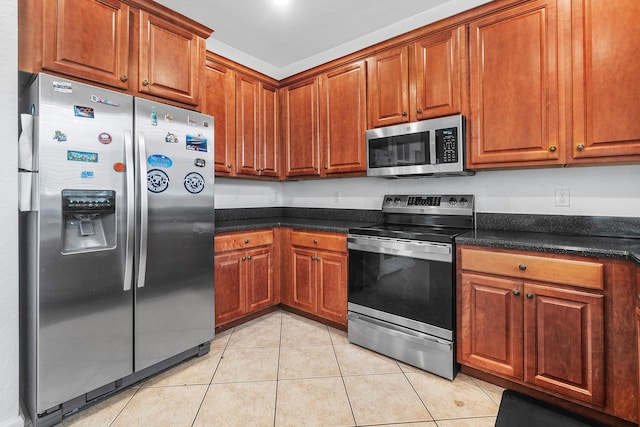 kitchen featuring light tile patterned floors, stainless steel appliances, brown cabinetry, and dark stone counters