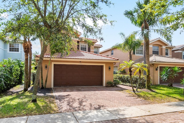 mediterranean / spanish house with an attached garage, a tiled roof, decorative driveway, and stucco siding