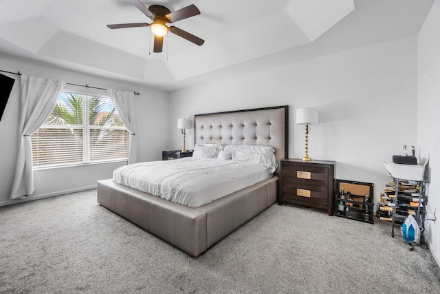 carpeted bedroom with a raised ceiling and a ceiling fan