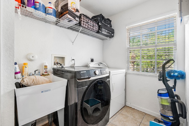 clothes washing area with washing machine and dryer, laundry area, a sink, and light tile patterned floors