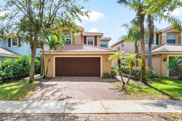 mediterranean / spanish-style house with a garage, decorative driveway, a tiled roof, and stucco siding