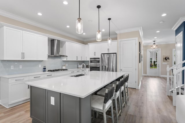 kitchen featuring ornamental molding, wall chimney exhaust hood, appliances with stainless steel finishes, and a sink