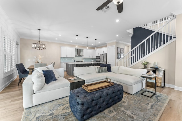 living area featuring baseboards, ornamental molding, stairs, light wood-style floors, and ceiling fan with notable chandelier