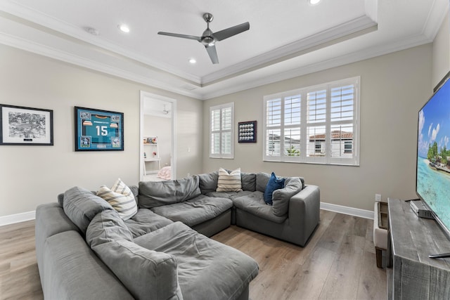 living room with a tray ceiling, a healthy amount of sunlight, and light wood-style flooring