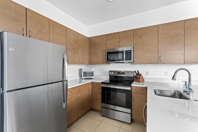 kitchen with light tile patterned floors, light countertops, appliances with stainless steel finishes, and a sink