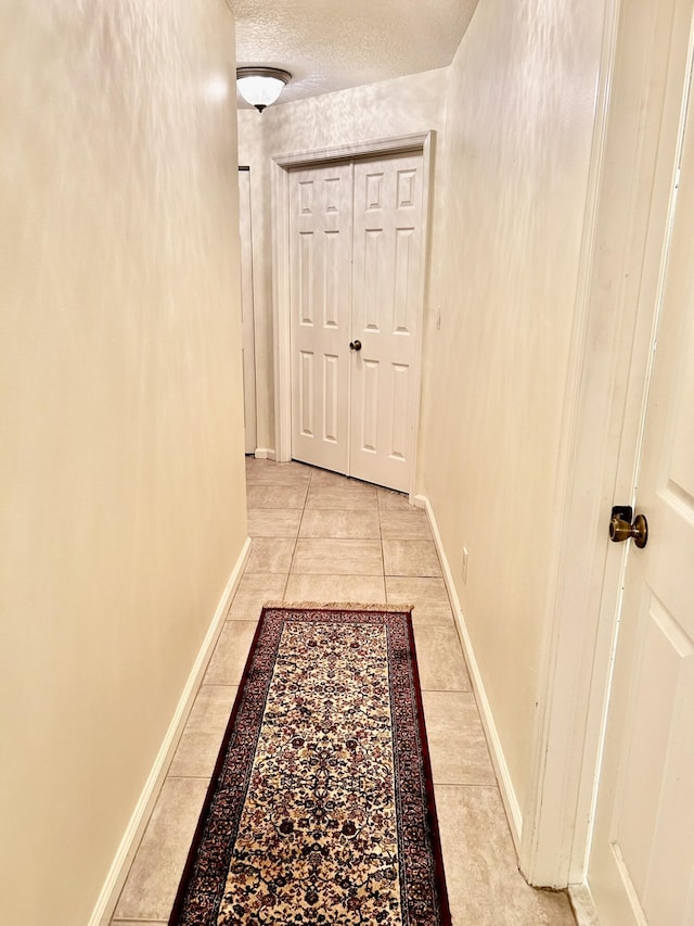 corridor featuring baseboards, a textured ceiling, and light tile patterned flooring