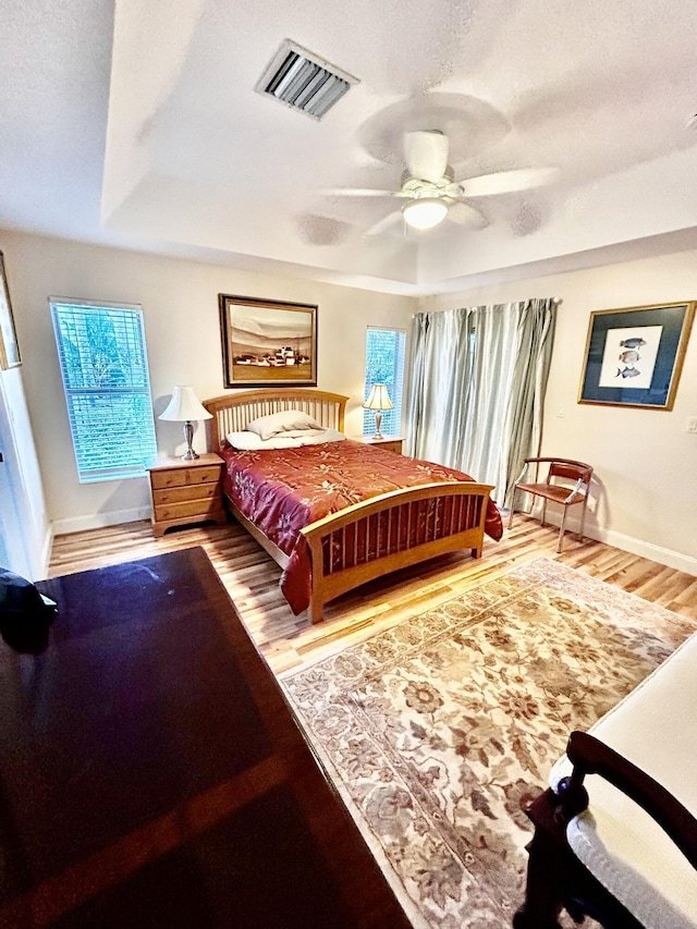 bedroom with a tray ceiling, visible vents, baseboards, and wood finished floors