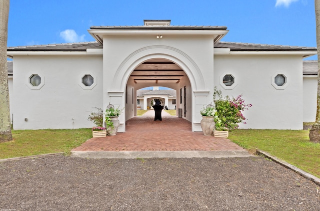 view of exterior entry featuring a tile roof, a yard, and stucco siding