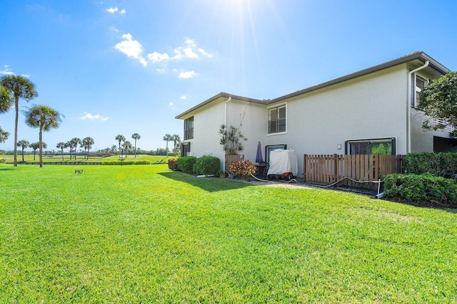 rear view of property featuring stucco siding, fence, and a yard