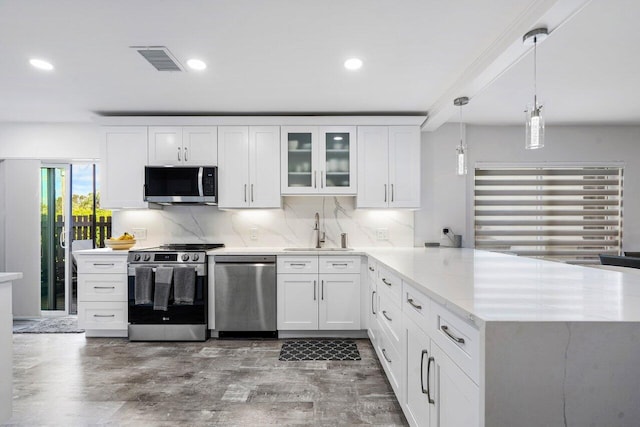 kitchen with visible vents, decorative backsplash, appliances with stainless steel finishes, a peninsula, and a sink