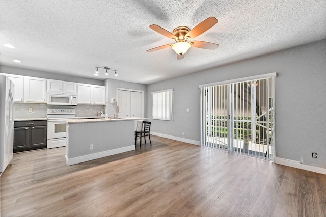 kitchen featuring white appliances, baseboards, a kitchen island with sink, decorative backsplash, and light wood-type flooring