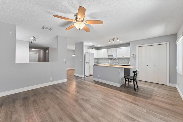 kitchen with light wood-style flooring, backsplash, white appliances, white cabinets, and light countertops