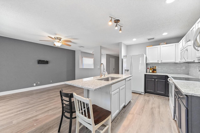 kitchen with light wood finished floors, a sink, decorative backsplash, white appliances, and a kitchen island with sink