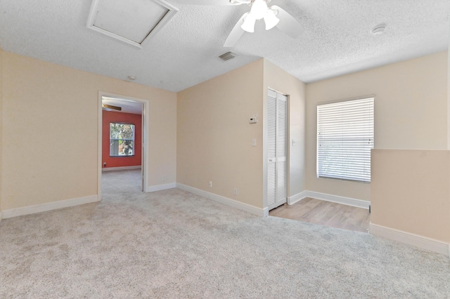 carpeted empty room with visible vents, a textured ceiling, attic access, and baseboards