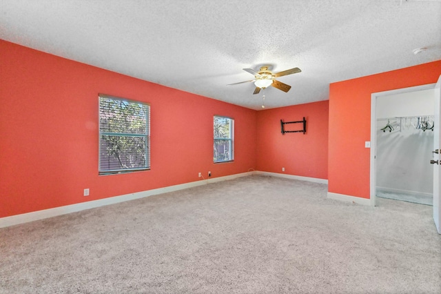 carpeted empty room with a ceiling fan, baseboards, and a textured ceiling