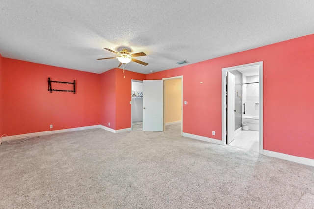 unfurnished bedroom with a textured ceiling, a spacious closet, baseboards, and light carpet