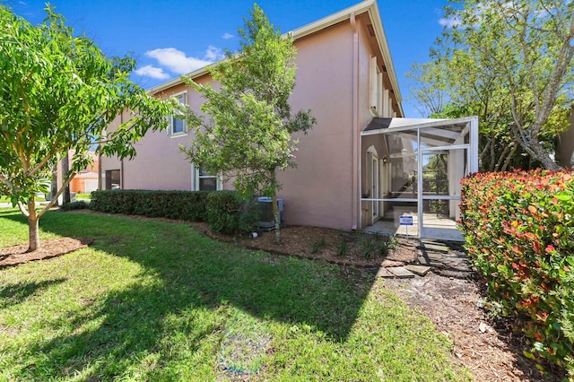 rear view of property with a yard, a sunroom, and stucco siding