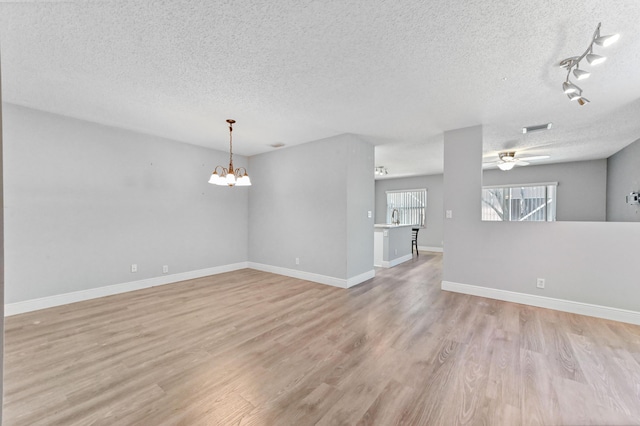 interior space featuring light wood finished floors, ceiling fan with notable chandelier, a textured ceiling, and baseboards