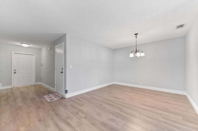 spare room with light wood finished floors, visible vents, a chandelier, and baseboards