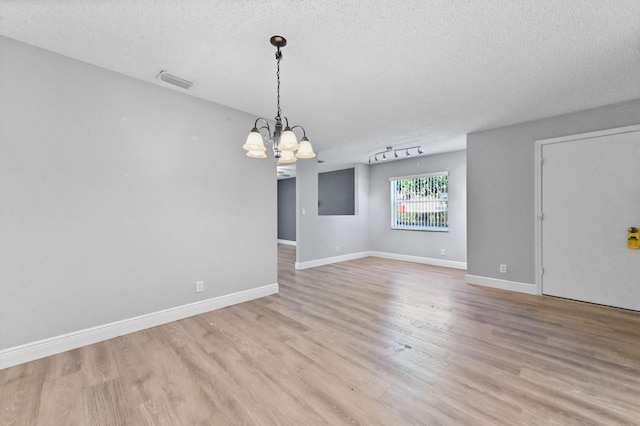 unfurnished room with visible vents, a textured ceiling, an inviting chandelier, light wood finished floors, and baseboards