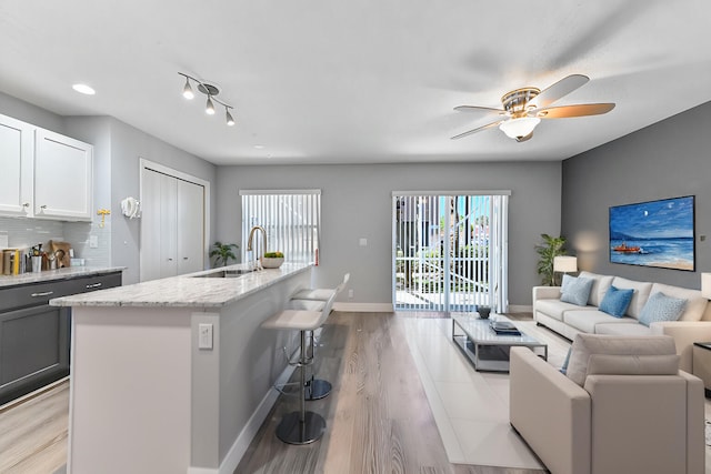 kitchen featuring baseboards, light wood finished floors, a sink, decorative backsplash, and open floor plan