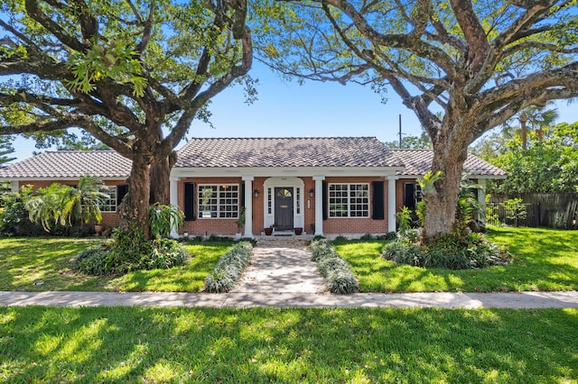 view of front of home featuring brick siding, fence, a tiled roof, and a front lawn