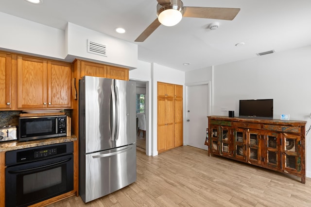 kitchen featuring freestanding refrigerator, black oven, visible vents, and light wood finished floors