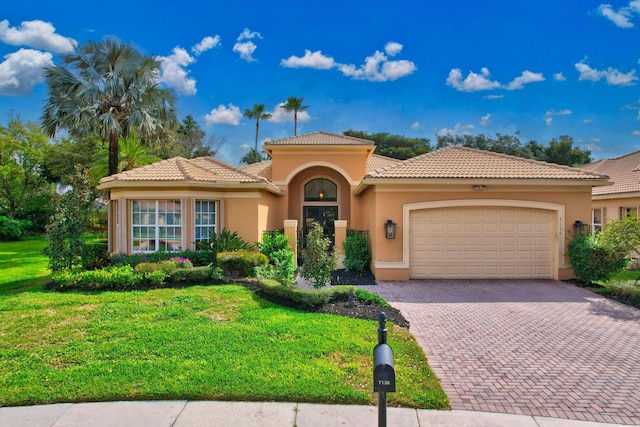 mediterranean / spanish-style home with a front lawn, a tiled roof, stucco siding, decorative driveway, and an attached garage