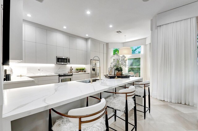 kitchen with visible vents, a breakfast bar, a sink, stainless steel appliances, and modern cabinets