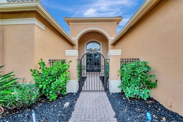 view of exterior entry with stucco siding, fence, and a gate