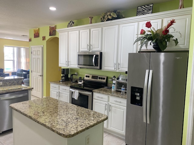 kitchen with light tile patterned floors, light stone counters, arched walkways, white cabinets, and stainless steel appliances