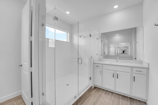 bathroom featuring a stall shower, baseboards, vanity, wood finish floors, and recessed lighting