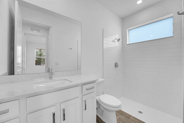 bathroom with toilet, vanity, visible vents, a tile shower, and a wealth of natural light