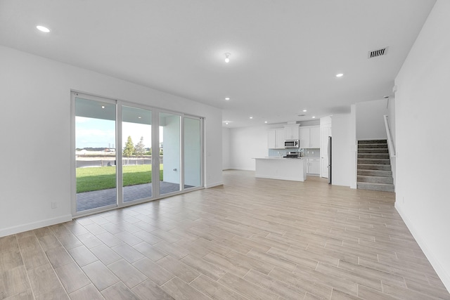 unfurnished living room with recessed lighting, visible vents, stairway, light wood-style floors, and baseboards