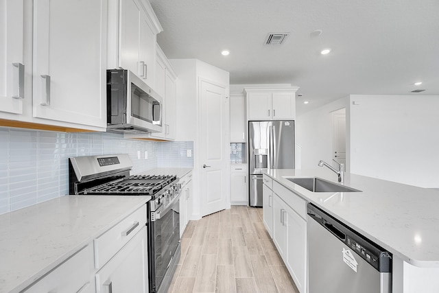 kitchen featuring a center island with sink, decorative backsplash, appliances with stainless steel finishes, white cabinetry, and a sink