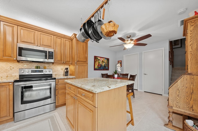 kitchen featuring light tile patterned floors, tasteful backsplash, appliances with stainless steel finishes, and a kitchen breakfast bar