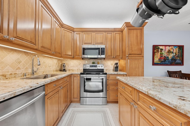 kitchen featuring appliances with stainless steel finishes, a sink, light stone counters, and tasteful backsplash