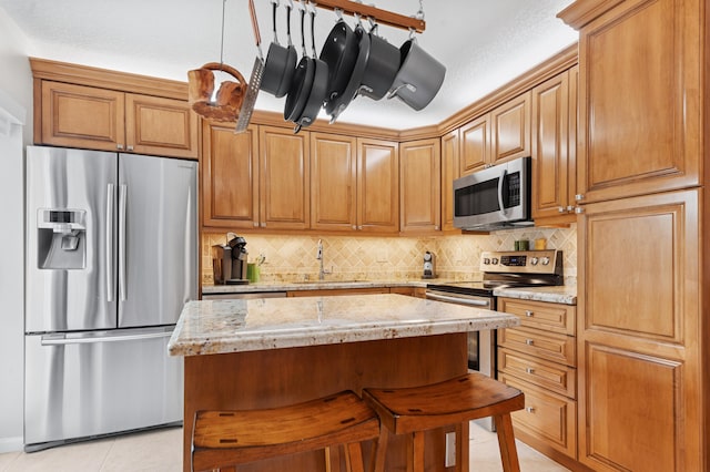 kitchen with decorative backsplash, appliances with stainless steel finishes, light tile patterned flooring, a sink, and light stone countertops