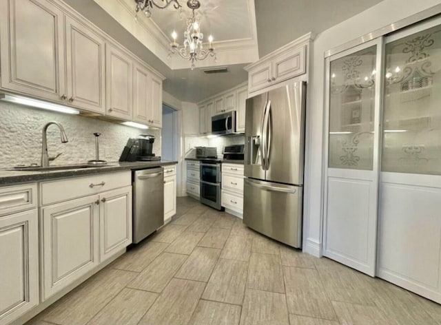 kitchen with dark countertops, a raised ceiling, appliances with stainless steel finishes, a sink, and a chandelier