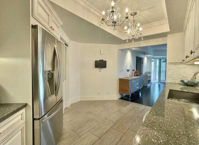 kitchen with a sink, stainless steel refrigerator with ice dispenser, wood tiled floor, a tray ceiling, and crown molding