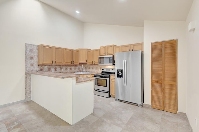 kitchen with appliances with stainless steel finishes, backsplash, a peninsula, and light brown cabinetry