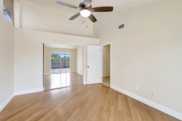 unfurnished bedroom featuring a towering ceiling, light wood-style floors, baseboards, and visible vents