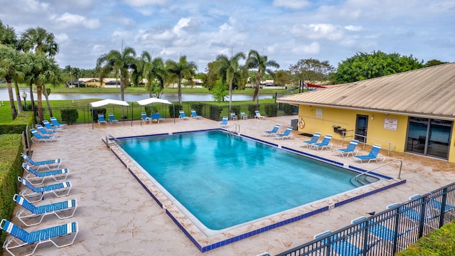 community pool with a patio, a water view, and fence