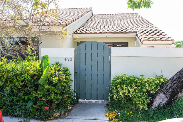 exterior space featuring a gate, fence, a tiled roof, and stucco siding